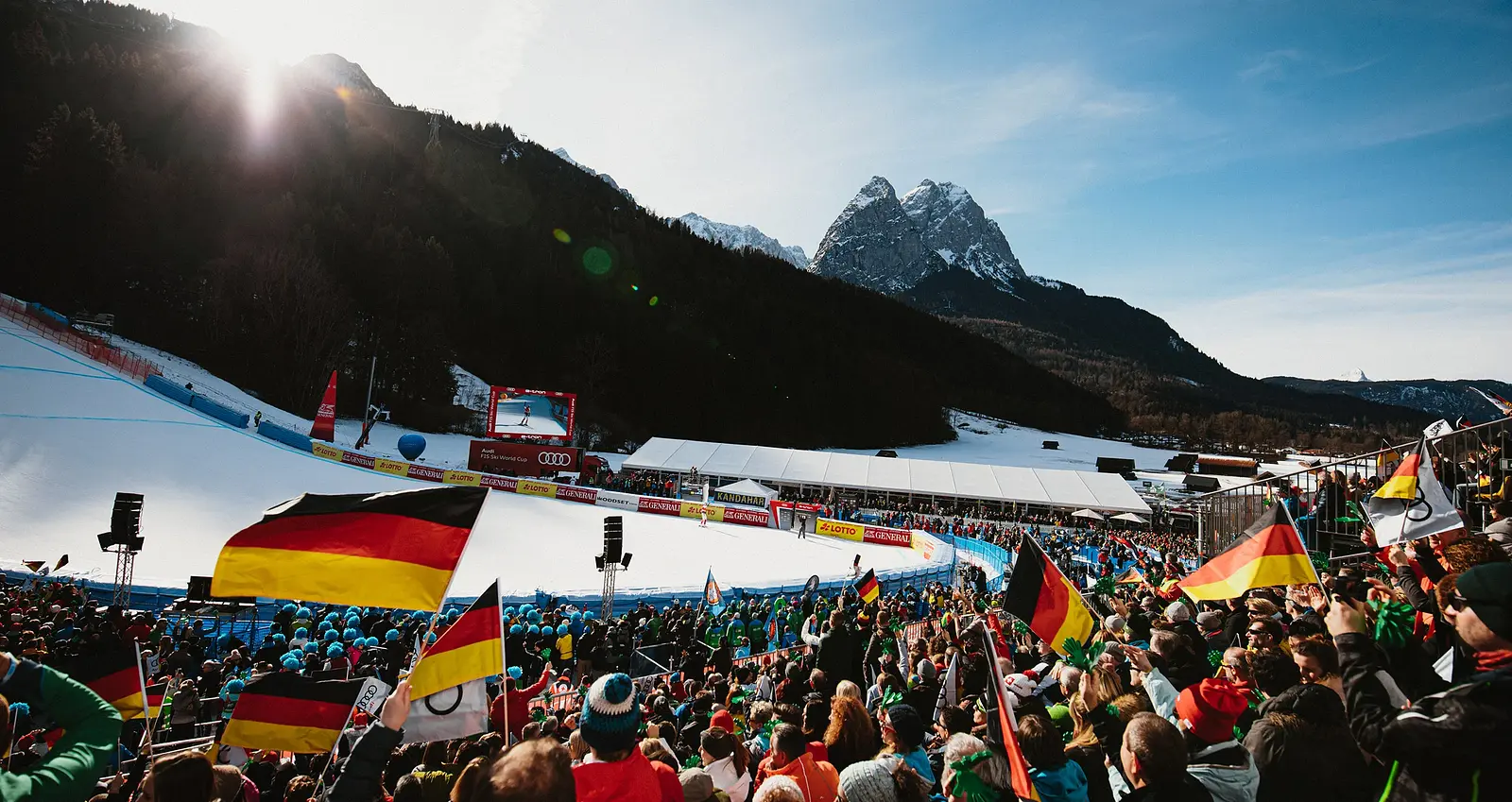 Foto vom Ski-Weltcup in Garmisch-Partenkirchen mit dicht besetzten Zuschauertribünen entlang der Kandahar-Abfahrt, zahlreichen Deutschlandfahnen im Publikum sowie verschneiter Rennstrecke vor Bergkulisse im Sonnenlicht