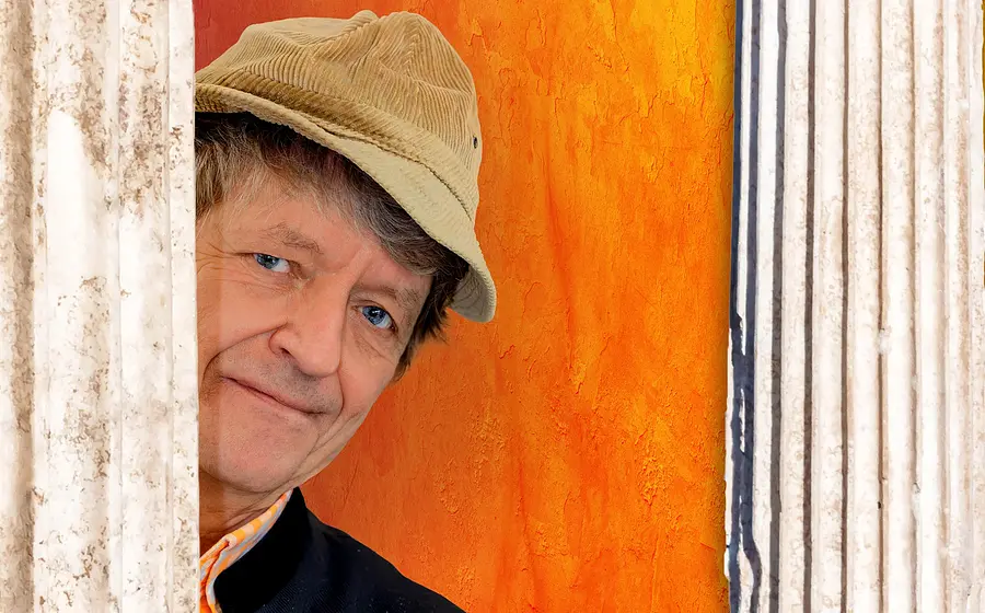 Foto von „Frank-Markus Barwasser“ mit orangefarbenem Hintergrund zwischen zwei Säulen