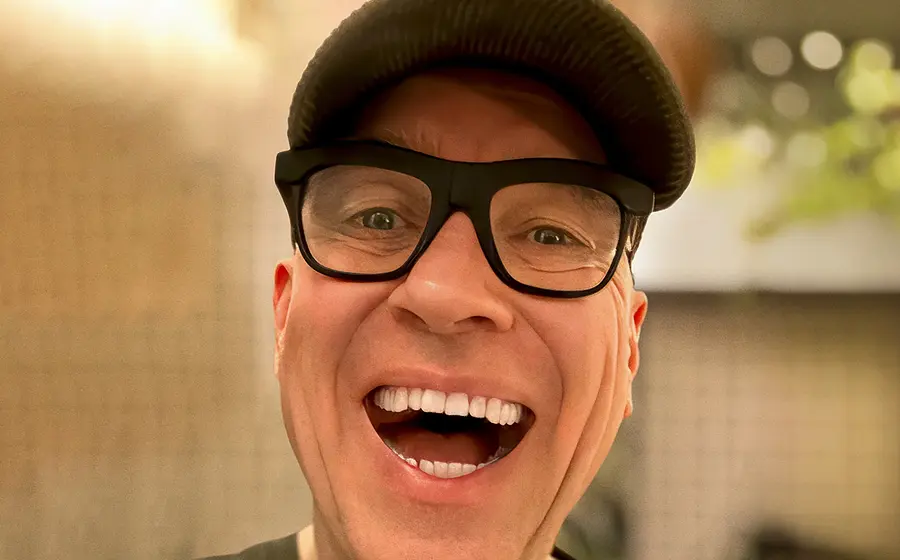 Der Künstler HG Butzko mit Brille und Kappe lacht in die Kamera