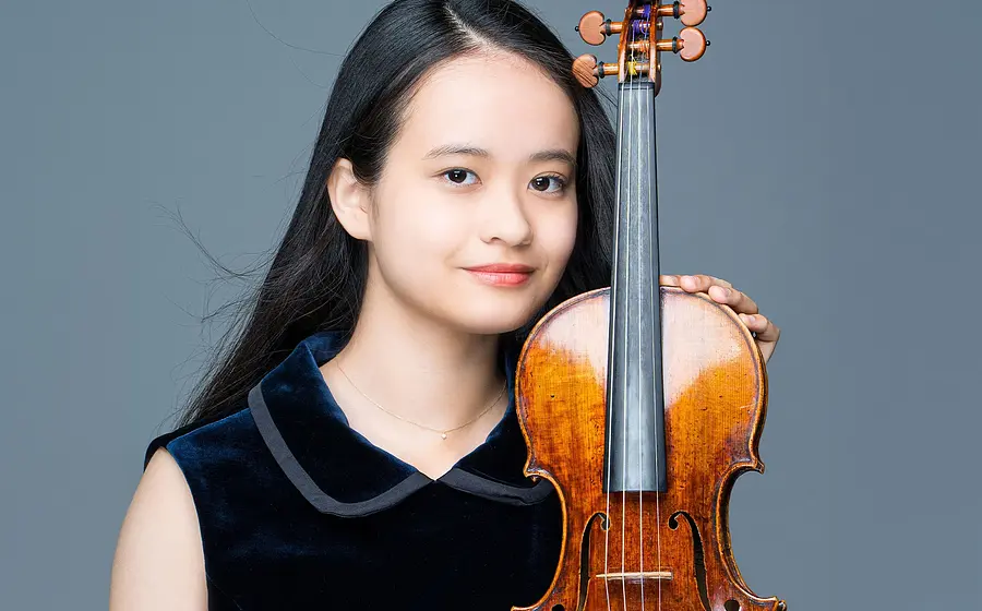 Porträt einer Person mit Violine vor grauem Hintergrund; die Violine wird aufrecht gehalten und steht im Vordergrund des Bildes.