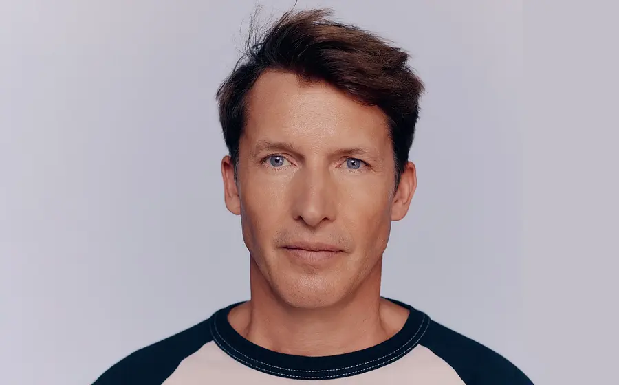 Portrait von James Blunt in einem blau-beigen Shirt vor hellem Hintergrund