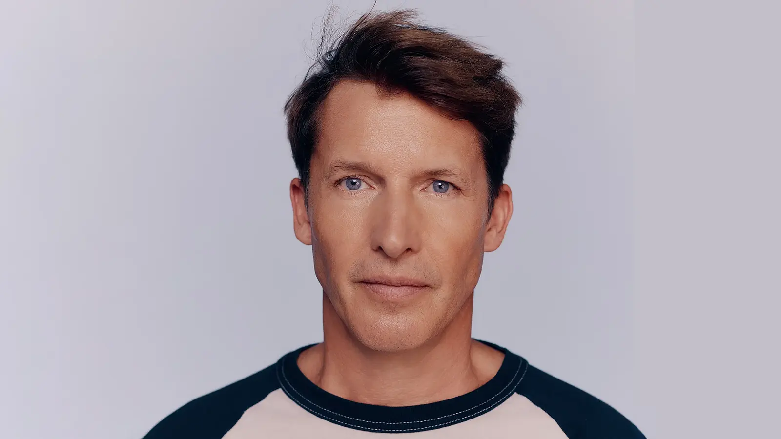 Portrait von James Blunt in einem blau-beigen Shirt vor hellem Hintergrund