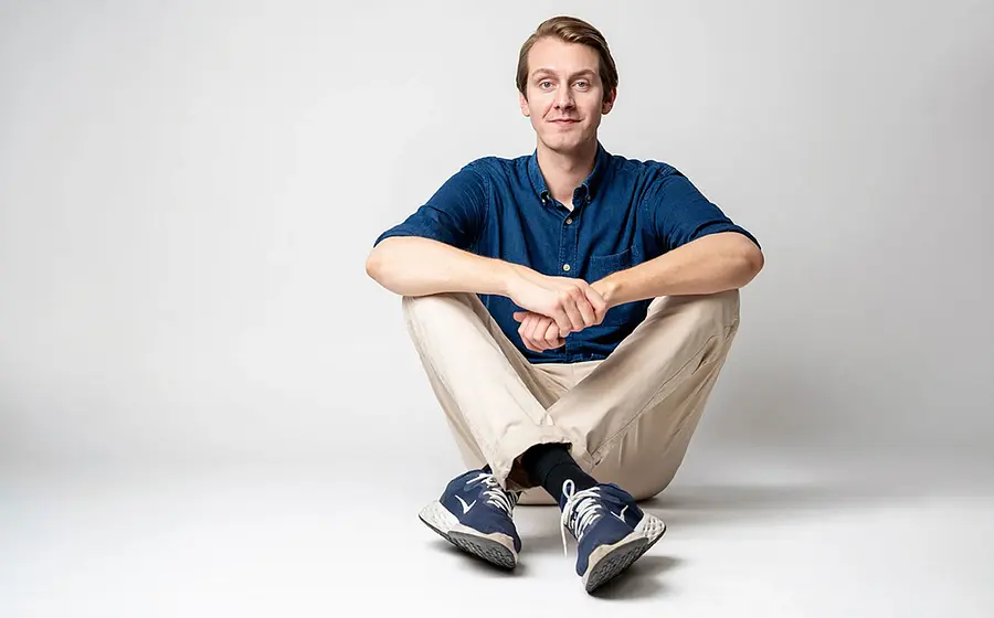 Foto zum Event ‚Jonas Greiner – Auf Augenhöhe‘: Der Künstler sitzt auf dem Boden vor grauem Hintergrund.