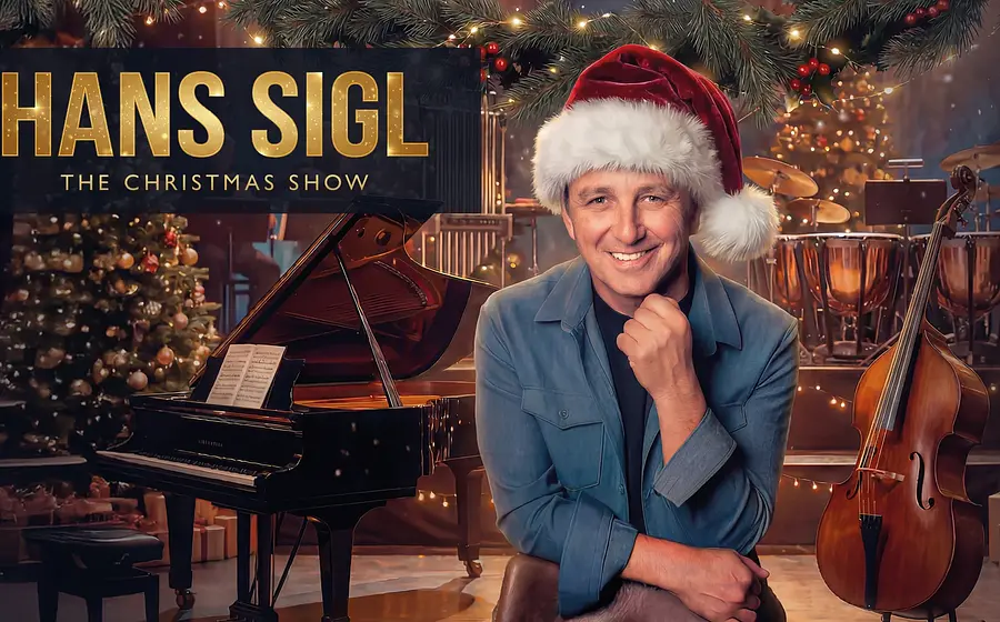 Eventmotiv zu „Hans Sigl – The Christmas Show“: Eine Person sitzt im Mittelpunkt eines festlich geschmückten Bühnenraums und trägt eine rote Weihnachtsmütze. Im Vordergrund stehen ein Flügel und ein Kontrabass, im Hintergrund sind Weihnachtsbaum, Lichterketten und Schlaginstrumente zu sehen. Warme Lichtstimmung mit goldenen und roten Akzenten. Oben links im Bild der Schriftzug „HANS SIGL – The Christmas Show“. Festliches Promomotiv für eine weihnachtliche Lesung mit Musik.
