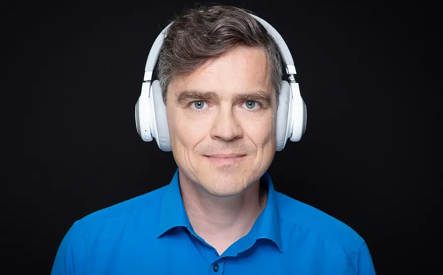 Henning Schmidtke in blauem Hemd mit weißem Kopfhörer vor schwarzem Hintergrund