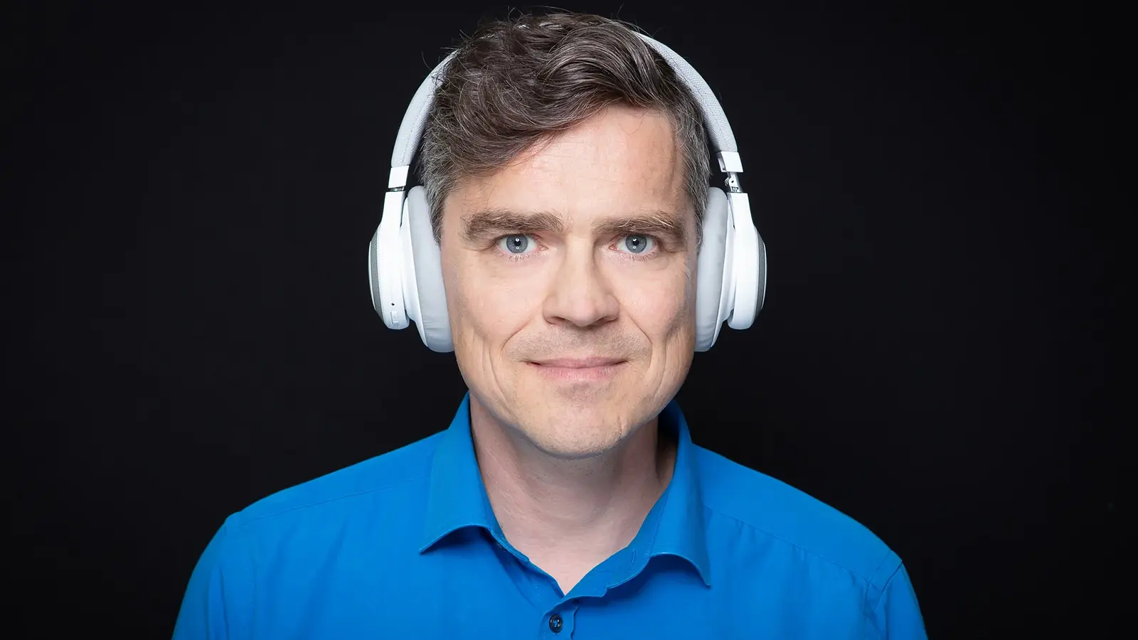 Henning Schmidtke in blauem Hemd mit weißem Kopfhörer vor schwarzem Hintergrund
