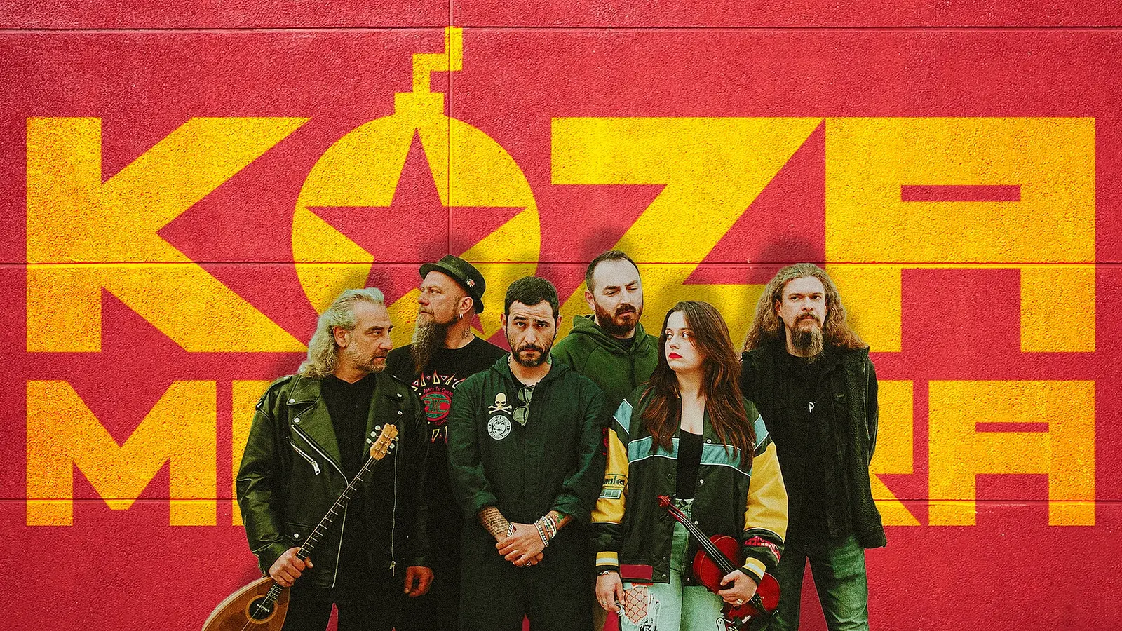 Sechs Personen stehen vor einer rot-gelben Wand mit großem ‚KOZA MOSTRA‘‑Schriftzug; einige halten Musikinstrumente wie Bouzouki und Geige, alle tragen legere bis rockige Kleidung
