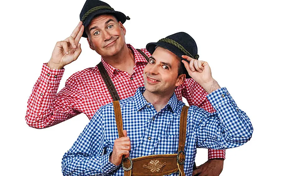 Zwei Personen in blau kariertem und rot kariertem Hemd mit braunen Lederhosen und dunklen Hüten vor hellem Hintergrund