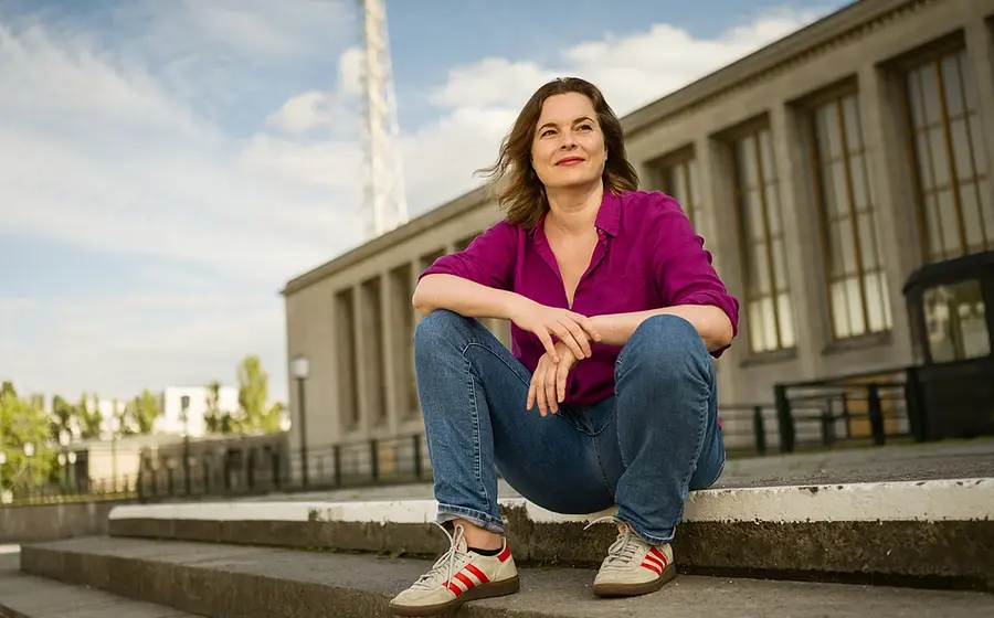 Katja Berlin sitzt draußen auf einer Treppe vor einem Gebäude und lächelt.