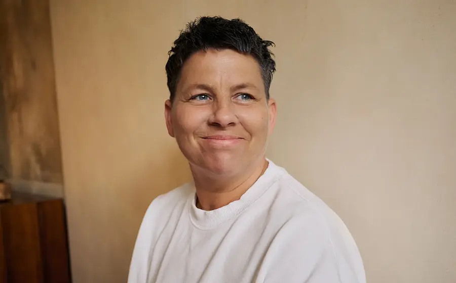 Kerstin Ott in weißem T-Shirt lächelnd, vor einer hellen Wand, auf der linken Seite eine Holzvertäfelung