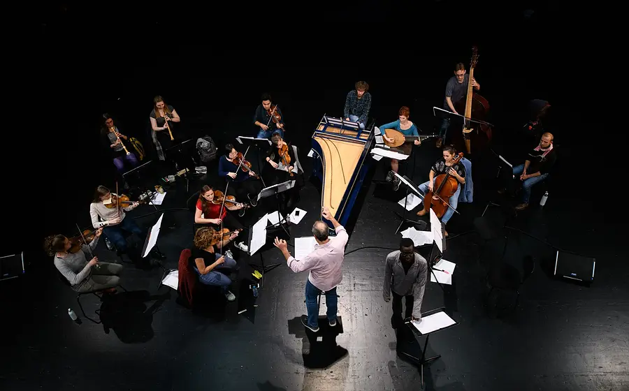 Bild eines Orchesters aus der Vogelperspektive mit Instrumenten auf einem schwarzen Bühnenboden stehend