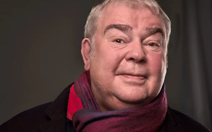 Portrait von Max Goldt mit rot-blauem Schal vor grauem Hintergrund