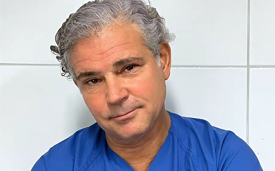 Foto von Michael Tsokos mit blauem Krankenhaushemd vor einer weißen Kachelwand wie im Krankenhaus