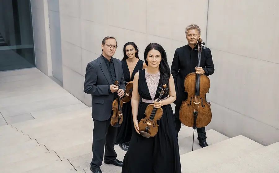Vier Musiker eines Streichquartetts stehen mit Violine, Viola und Violoncello in einem modernen architektonischen Raum