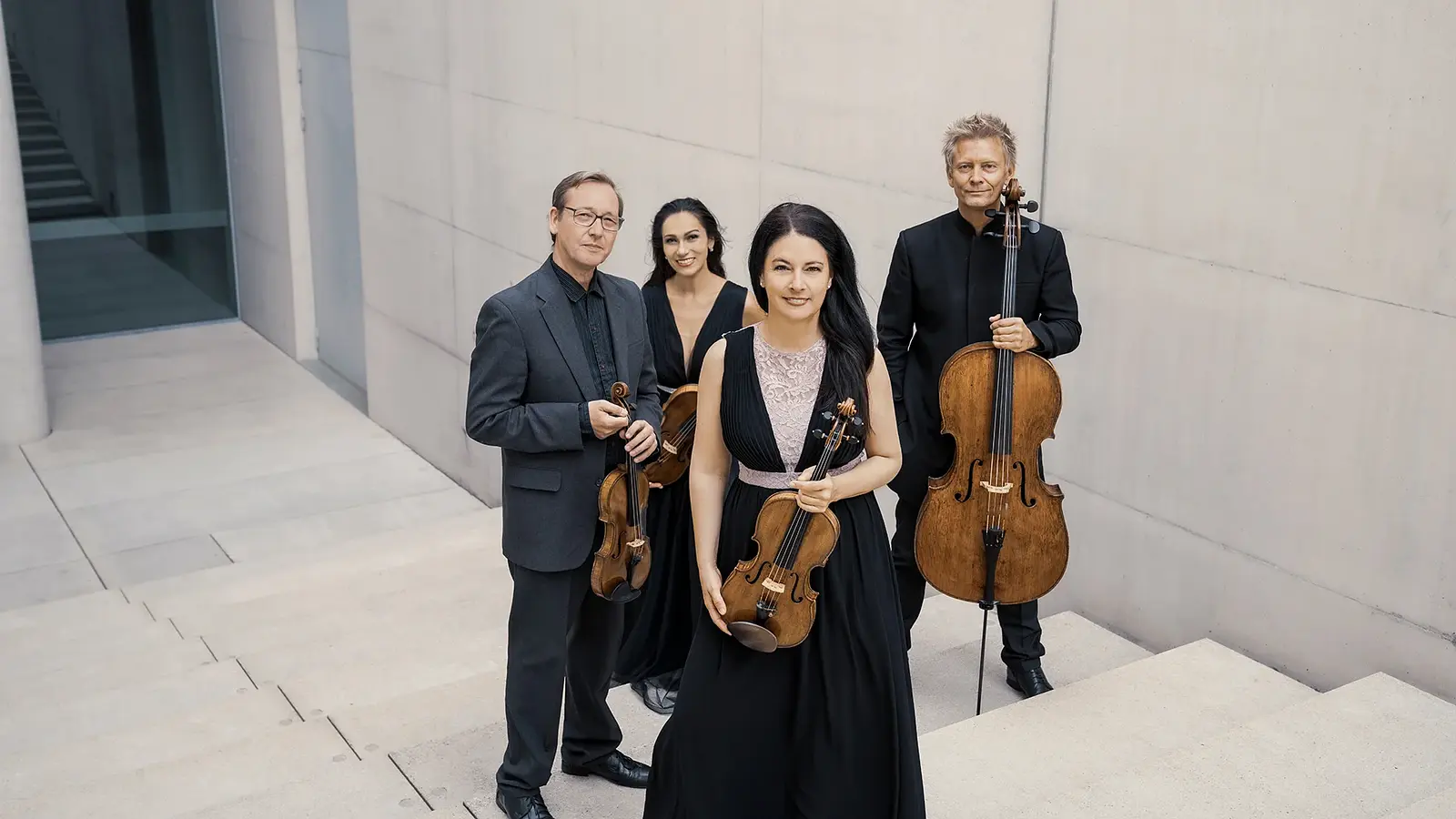 Vier Musiker eines Streichquartetts stehen mit Violine, Viola und Violoncello in einem modernen architektonischen Raum