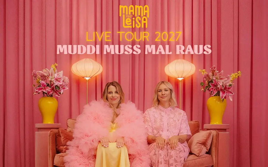 Plakat Mama Leisa Live Tour 2027 Muddi muss mal raus mit zwei Personen in rosafarbener Kleidung auf einem Sofa vor pinkem Vorhang, links und rechts Stehlampen und gelben Vasen mit Blumen.