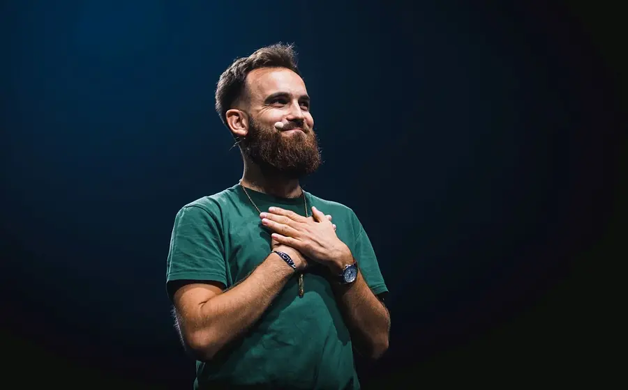 Maik Baum mit gekreuzten Händen in einem dunkelgrünen Shirt vor dunklem Hintergrund