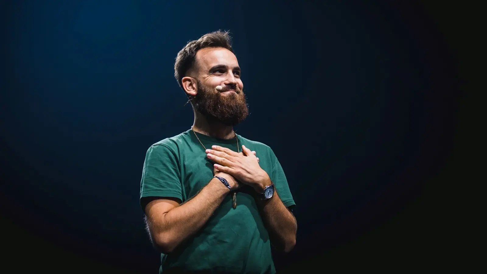 Maik Baum mit gekreuzten Händen in einem dunkelgrünen Shirt vor dunklem Hintergrund