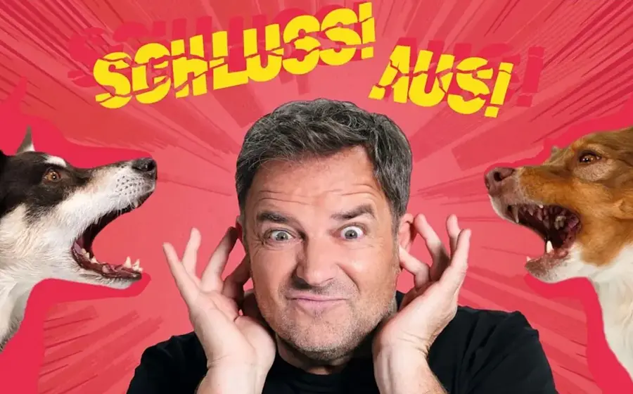 Foto von Martin Rütter, wie er sich die Ohren zuhält, während zwei Hunde an den Seiten bellen, vor rotem Hintergrund