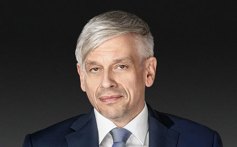 Mathias Tretter in dunkelblauem Anzug mit weißem Hemd und blauer Krawatte vor dunkelgrauem Hintergrund