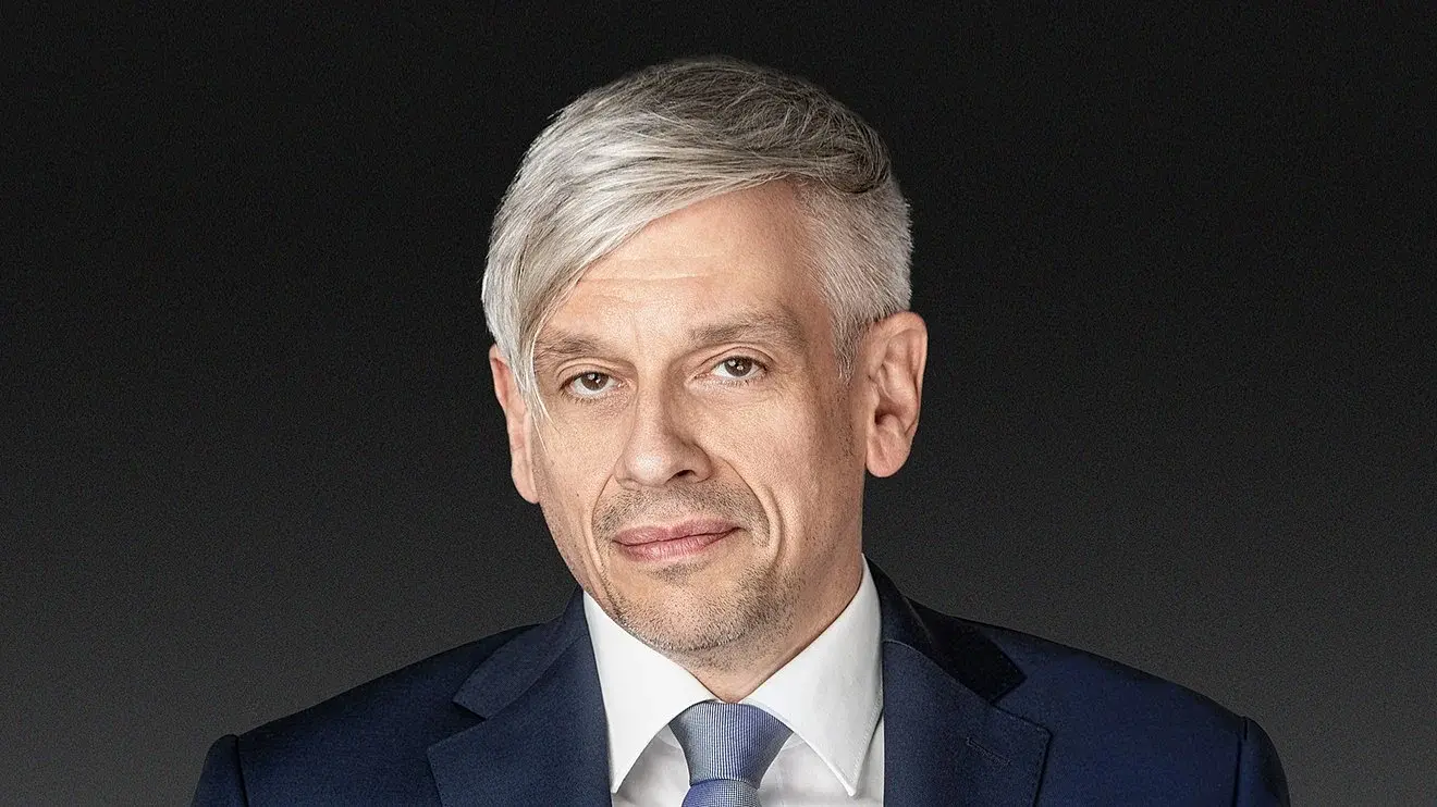 Mathias Tretter in dunkelblauem Anzug mit weißem Hemd und blauer Krawatte vor dunkelgrauem Hintergrund