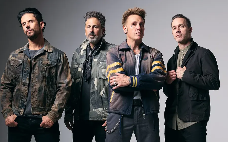 Bandfoto von Papa Roach: Vier Musiker stehen nebeneinander vor grauem Hintergrund, tragen dunkle Kleidung im Rockstil; einer im Vordergrund mit verschränkten Armen.