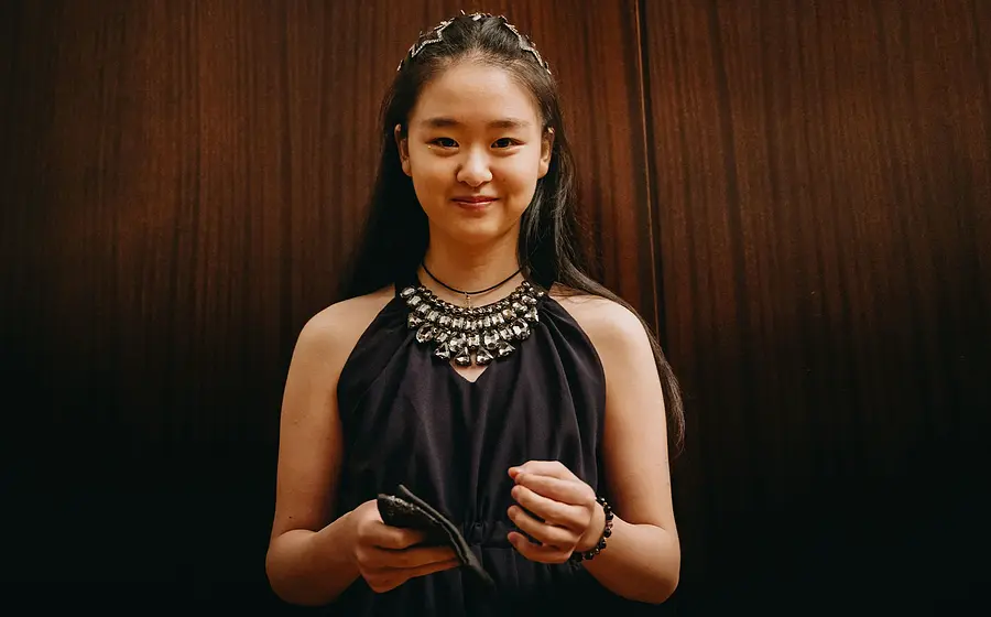 Die Pianistin Tianyao Lyu in schwarzer festlicher Kleidung mit dominanter Halskette lächelnd vor braunem Hintergrund