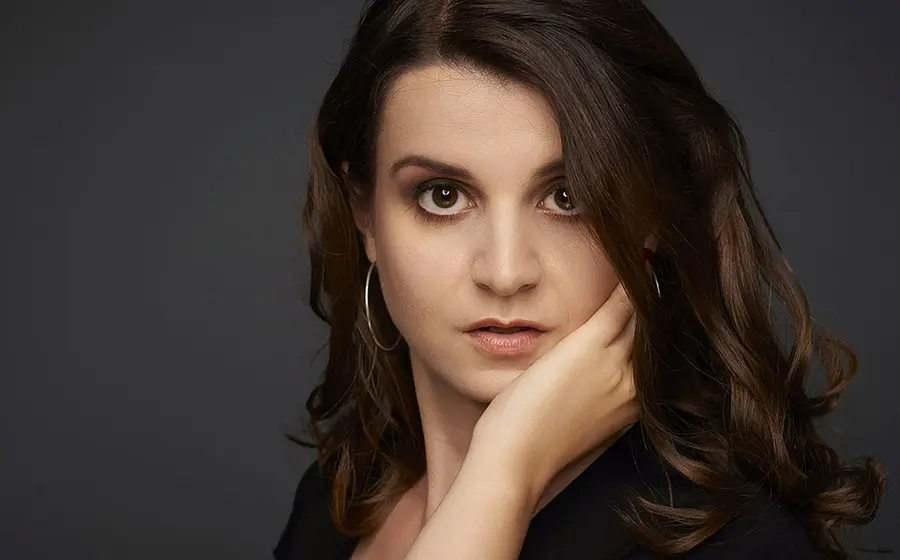 Portrait einer Dame mit dunklen langen Haaren, die das Kinn auf die Hand stützt, vor dunklem Hintergrund