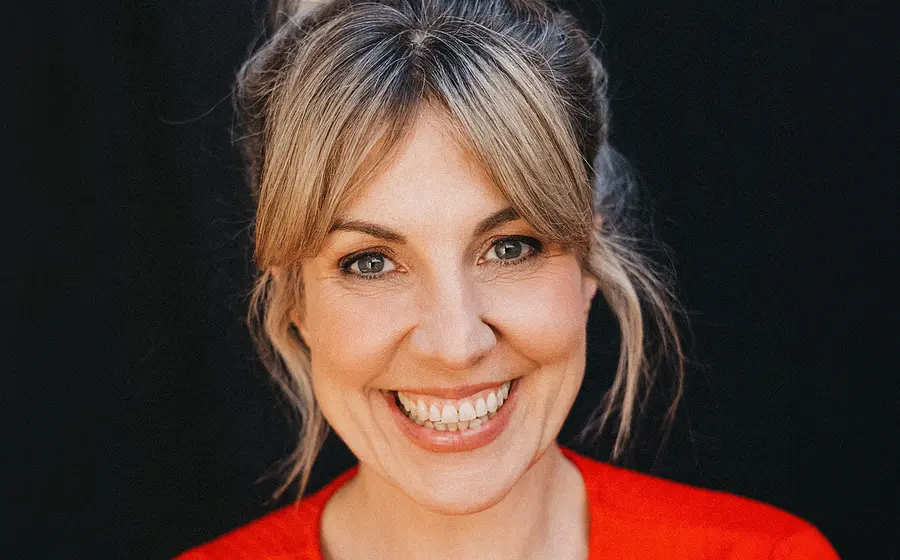 Portrait von Nora Boeckler in einem knallig rotem Oberteil, wie sie gerade in die Kamera blickt vor einem schwarzem Hintergrund