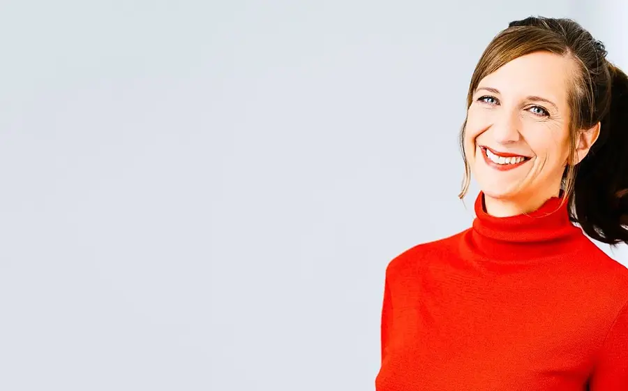 Sarah Hakenberg steht mit einem roten Pulli vor einer weißen Wand