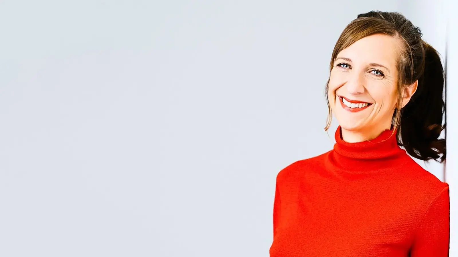 Sarah Hakenberg steht mit einem roten Pulli vor einer weißen Wand