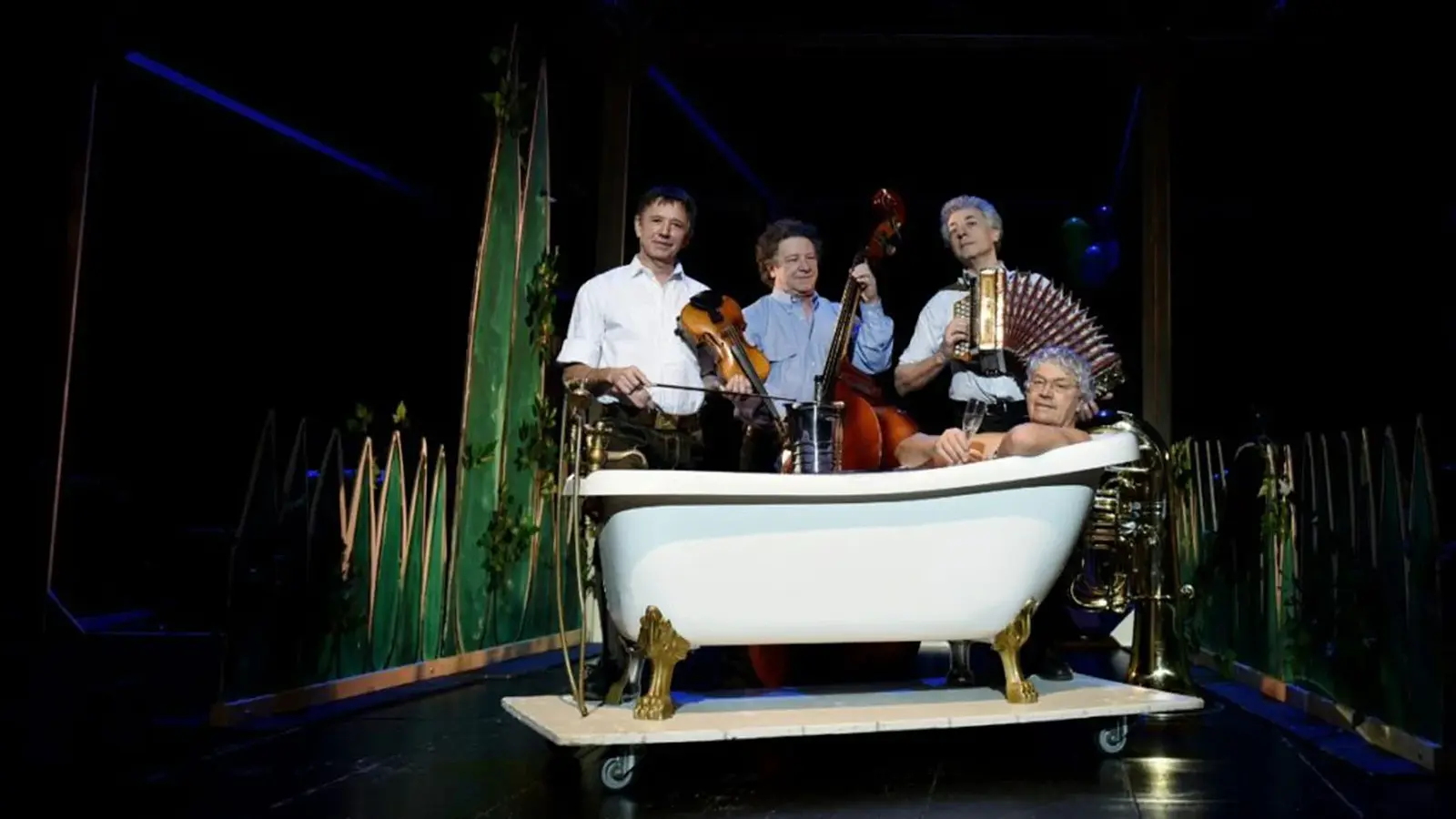 Veranstaltungsfoto von ‚Well Brüder & Wellküren – Familienbande‘ mit Ensemble auf der Bühne und einem Darsteller in einer Badewanne.