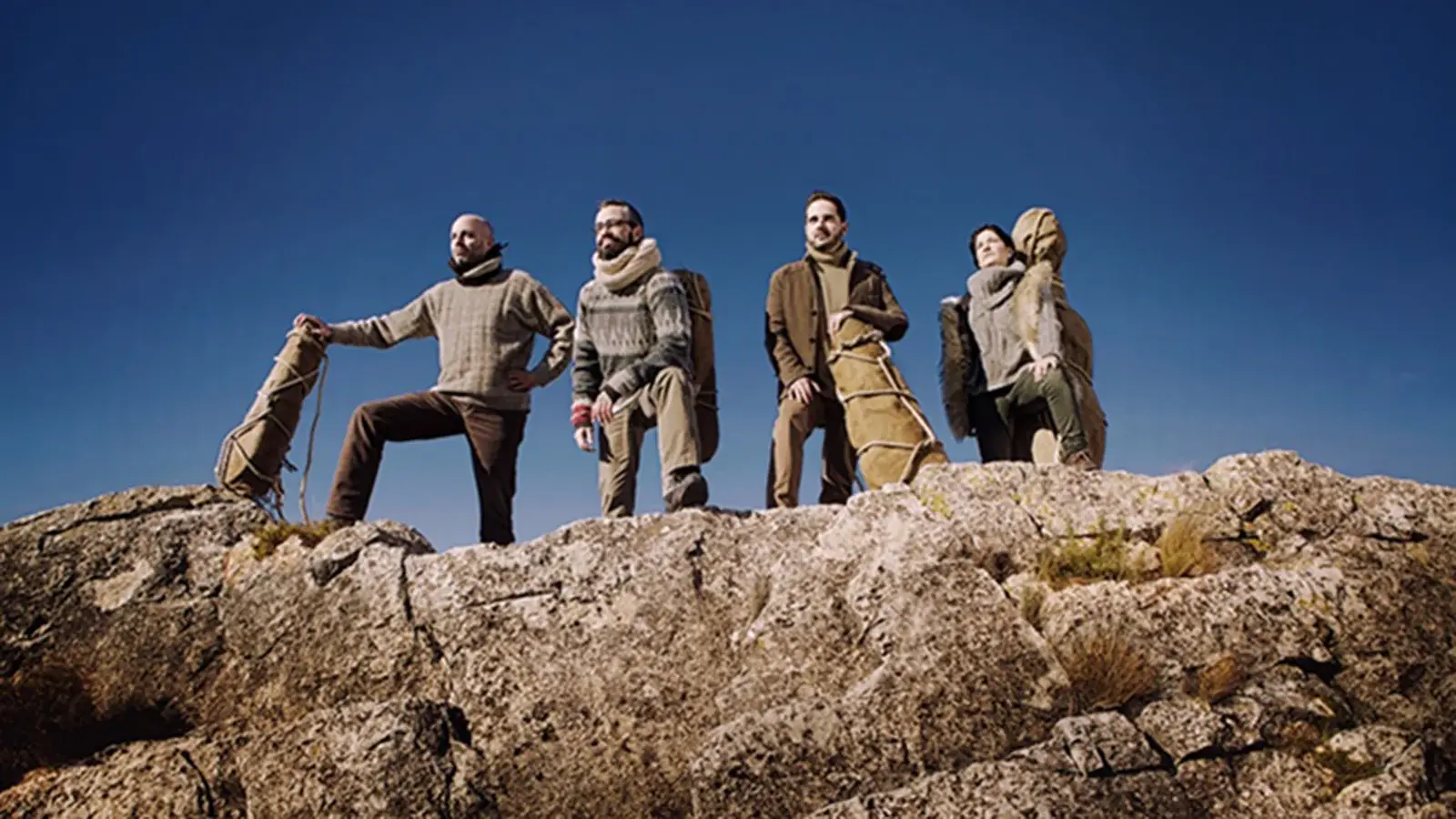 Personengruppe auf einer felsigen Anhöhe mit Instrumentenkoffern vor klarem blauem Himmel. Die Mitglieder des Quiroga Quartetts stehen in Outdoor-Kleidung auf einem Felsrücken und blicken in die Ferne