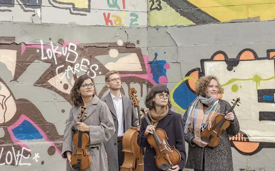 Streichquartett mit vier Musikerinnen und Musikern vor einer bunt bemalten Graffitiwand. Die Mitglieder des Chaos String Quartet halten Violinen und Violoncello und stehen vor urbaner Streetart-Kulisse.
