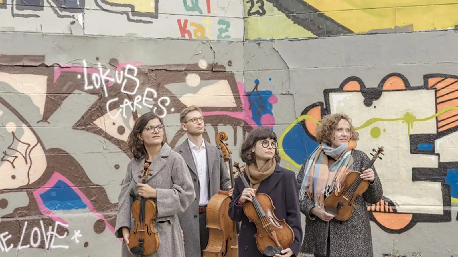 Streichquartett mit vier Musikerinnen und Musikern vor einer bunt bemalten Graffitiwand. Die Mitglieder des Chaos String Quartet halten Violinen und Violoncello und stehen vor urbaner Streetart-Kulisse.