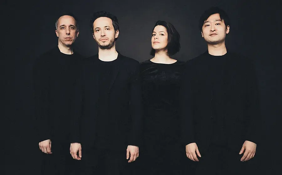 Quatuor Ébène mit vier Personen in dunkler Kleidung vor schwarzem Hintergrund, nebeneinander stehend in einer Studioaufnahme ohne sichtbare Instrumente.
