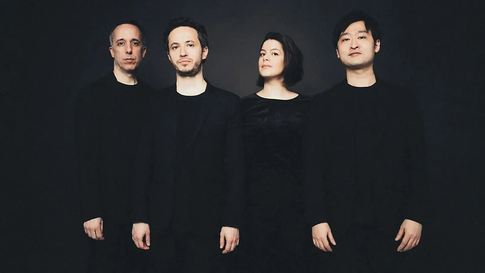 Quatuor Ébène mit vier Personen in dunkler Kleidung vor schwarzem Hintergrund, nebeneinander stehend in einer Studioaufnahme ohne sichtbare Instrumente.