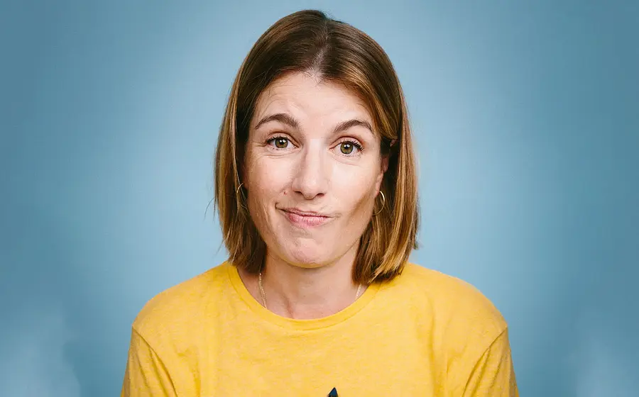 Foto für die Veranstaltung von Suse Lichtenberger mit der Künstlerin im gelben T‑Shirt vor blauem Hintergrund