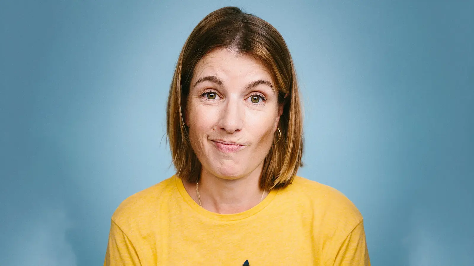 Foto für die Veranstaltung von Suse Lichtenberger mit der Künstlerin im gelben T‑Shirt vor blauem Hintergrund