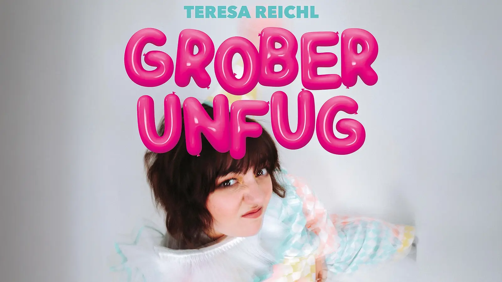Die Künstlerin Theresa Reichl mit Grimasse und pinker Aufschrift Grober Unfug vor hellgrau verschwommenem Hintergrund