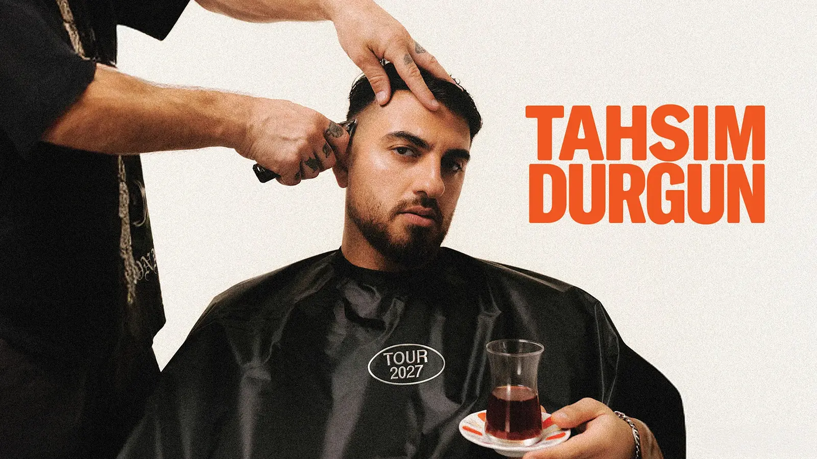 Plakat von Tahsim Durgun beim Haareschneiden, sitzend mit Friseurumhang und Teeglas in der Hand, daneben der Schriftzug Tahsim Durgun und Tour 2027