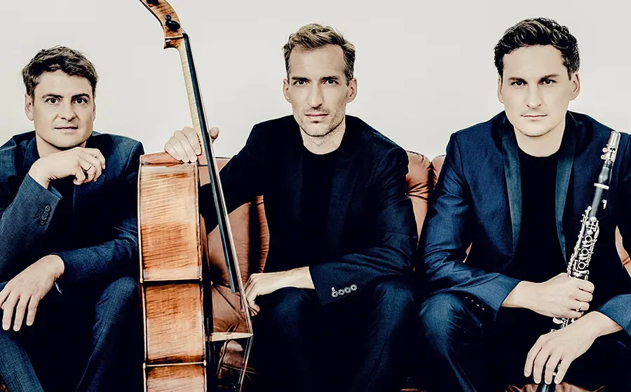 Drei Musiker des Clarinet Trio sitzen auf einem Sofa. Einer hält ein Violoncello, ein anderer eine Klarinette