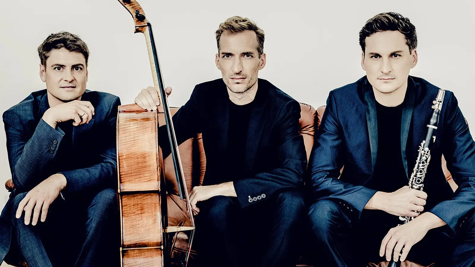 Drei Musiker des Clarinet Trio sitzen auf einem Sofa. Einer hält ein Violoncello, ein anderer eine Klarinette