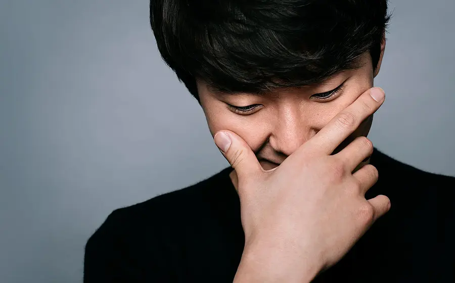Porträtmotiv von Seong‑Jin Cho: Der Pianist ist in enger Nahaufnahme zu sehen und hält eine Hand vor das Gesicht, der Kopf ist leicht nach unten geneigt. Er trägt ein dunkles Oberteil. Neutraler grauer Studiohintergrund ohne weitere Elemente. Weiches, gerichtetes Licht betont Gesicht und Hand. Ruhiges, konzentriertes Promofoto für einen klassischen Klavierabend mit Seong‑Jin Cho.
