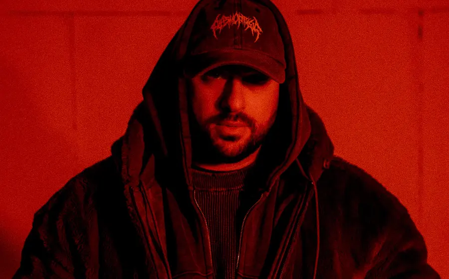 Portrait in schwarz/rot des Künstlers Timey mit Kapppe und dunkler Kleidung sowie Kapuze
