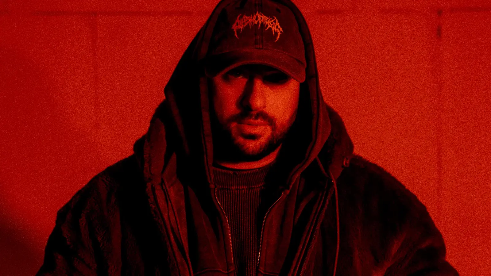 Portrait in schwarz/rot des Künstlers Timey mit Kapppe und dunkler Kleidung sowie Kapuze