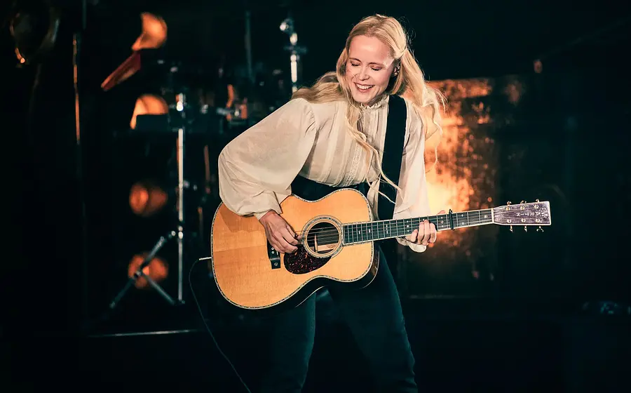 Foto für die Veranstaltung „TINA DICO“ mit der Künstlerin auf der Bühne während eines Auftritts, mit einer Gitarre in der Hand.