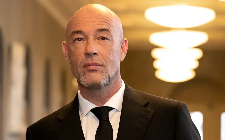 Ein Portrait des Künstlers in eine schwarzen Anzug in einem Flur mit Deckenbeleuchtung