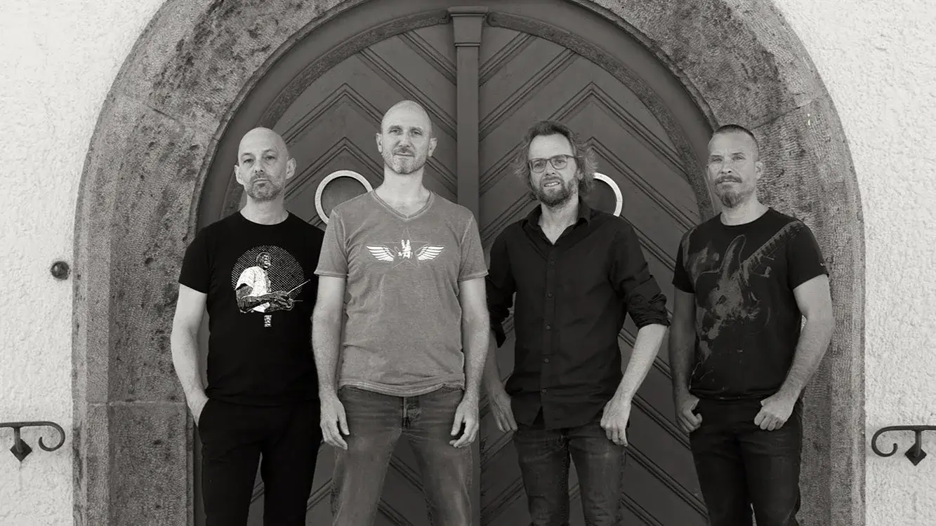 Pressefoto des Vlado Grizelj Quartetts mit vier Musikern vor einem großen Rundbogenportal, in Schwarzweißaufnahme mit dunkler Freizeitkleidung vor einer historischen Tür.