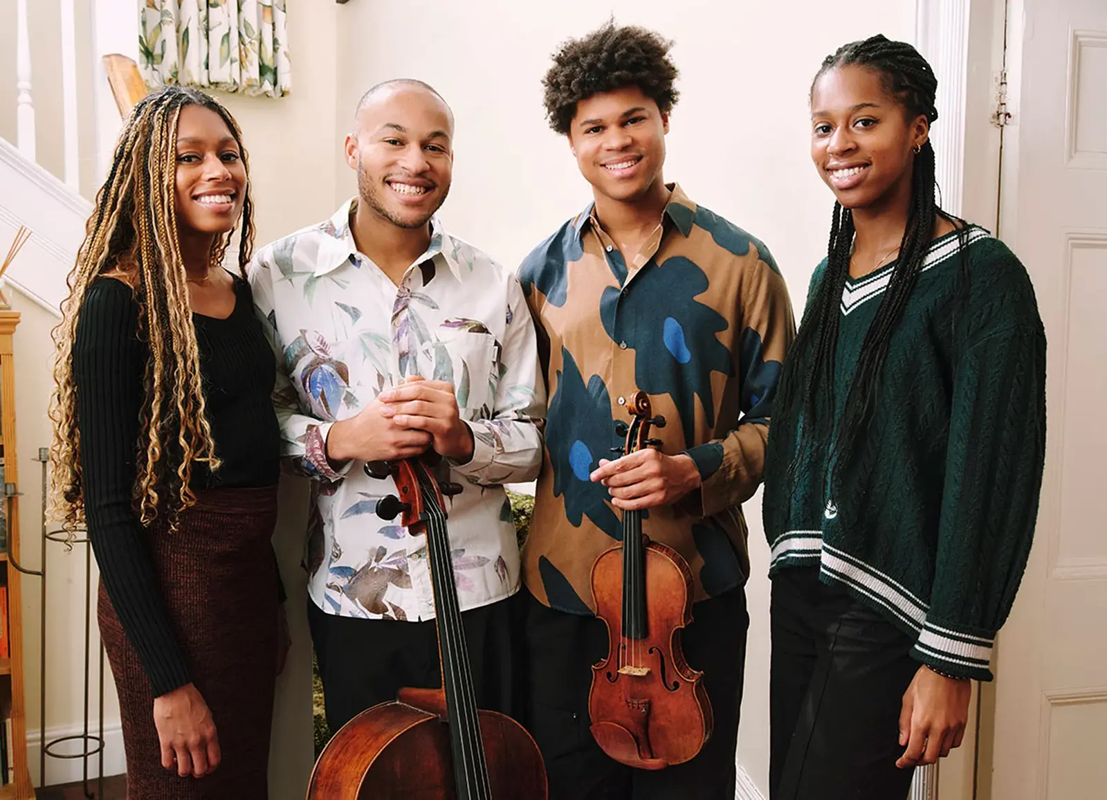 Die vier Mitglieder der Kanneh Masons lachend in bunter Kleidung, zwei Personen mit Instrumenten, vor hellem Hintergrund